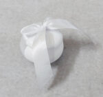 Μπομπονιέρα γάμου κεραμική σε σχήμα μακαρόν δεμένη με λευκή σατέν κορδέλα.