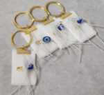 Μαρτυρικά βάπτισης μπρελόκ με  λευκή βελούδινη κορδέλα, πούπουλα και παραμάνα με μπλέ ματάκι χάντρα.