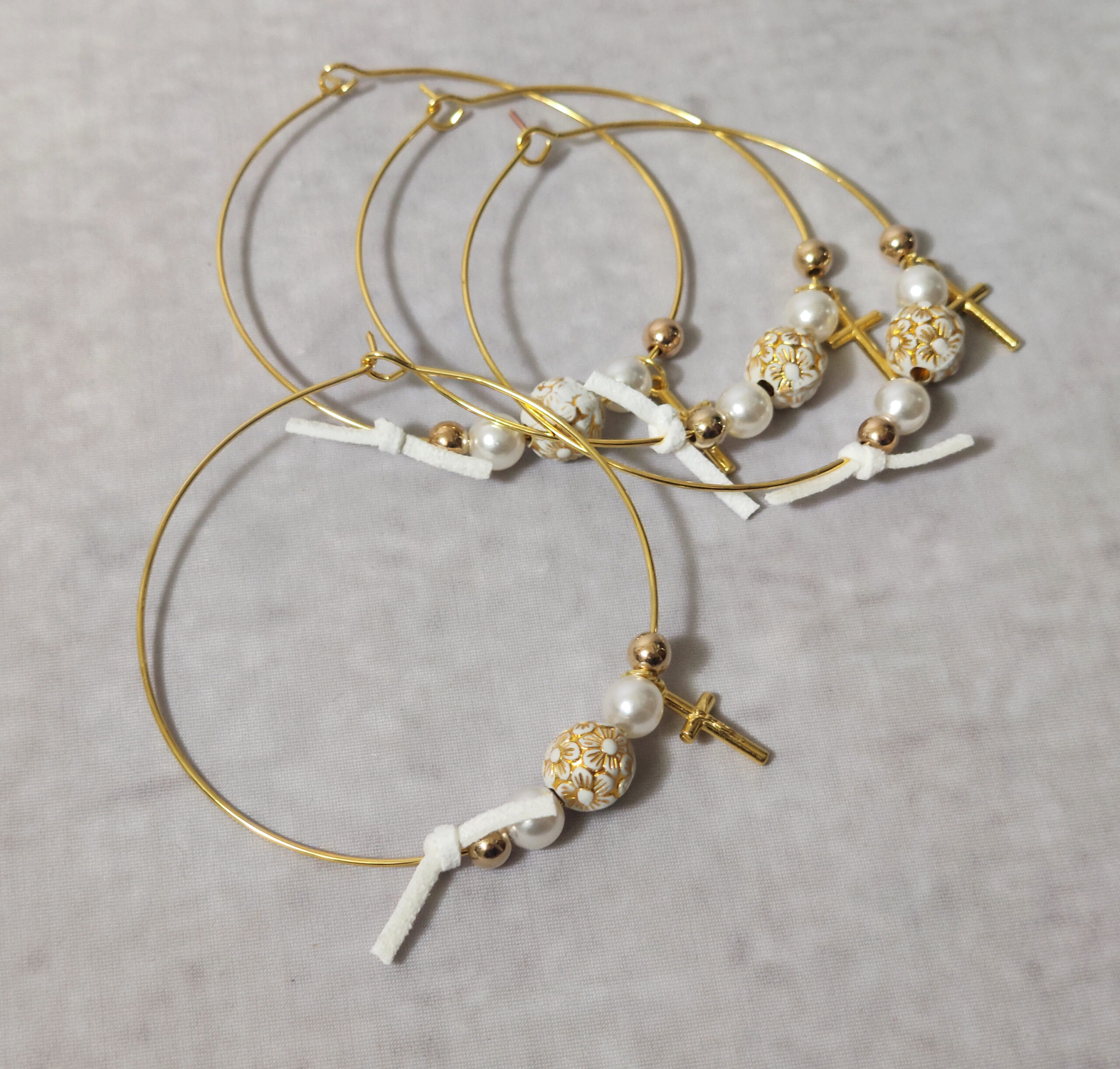 Μαρτυρικά βάπτισης μεταλλικά βραχιόλια στολισμένα με 2 λευκές πέρλες, περίτεχνη χάντρα με χάραξη λουλούδια, 2 χρυσές χάντρες με μεταλλικό χρυσό σταυρό και δερμάτινο λευκό φιογκάκι.