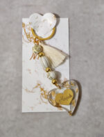 Μαρτυρικά βάπτισης μπρελόκ με λευκές και χρυσές χάντρες, καρδούλα με χάραξη από χρυσό καθρέφτη πλεξι γκλας και διακοσμητικό από υγρό γυαλί με φύλλα χρυσού και καρδιά από χρυσό καθρέφτη πλεξι γκλας.