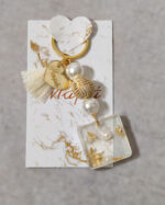 Μαρτυρικά βάπτισης μπρελόκ με λευκές και χρυσές χάντρες, καρδούλα με χάραξη από χρυσό καθρέφτη πλεξι γκλας και διακοσμητικό από υγρό γυαλί με πέρλα και φύλλα χρυσού.