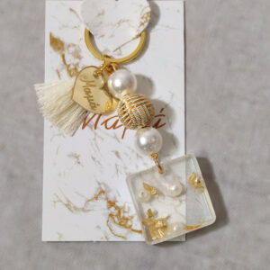 Μαρτυρικά βάπτισης μπρελόκ με λευκές και χρυσές χάντρες, καρδούλα με χάραξη από χρυσό καθρέφτη πλεξι γκλας και διακοσμητικό από υγρό γυαλί με πέρλα και φύλλα χρυσού.